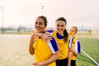 Three school aged females laughing on a soccer pitch