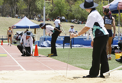 three athletics offials measure at the long jump pit