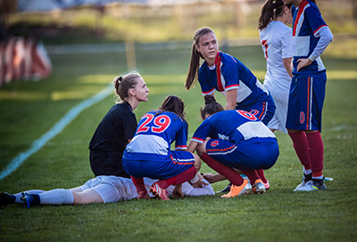 Female football player lying on the ground with team mates around her